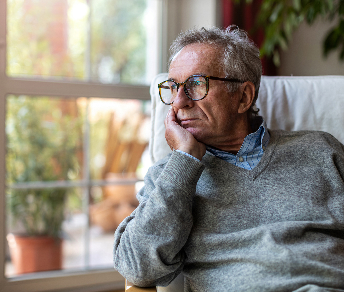 Senior man looking out of window at home Senior man next to a window, deep in thought