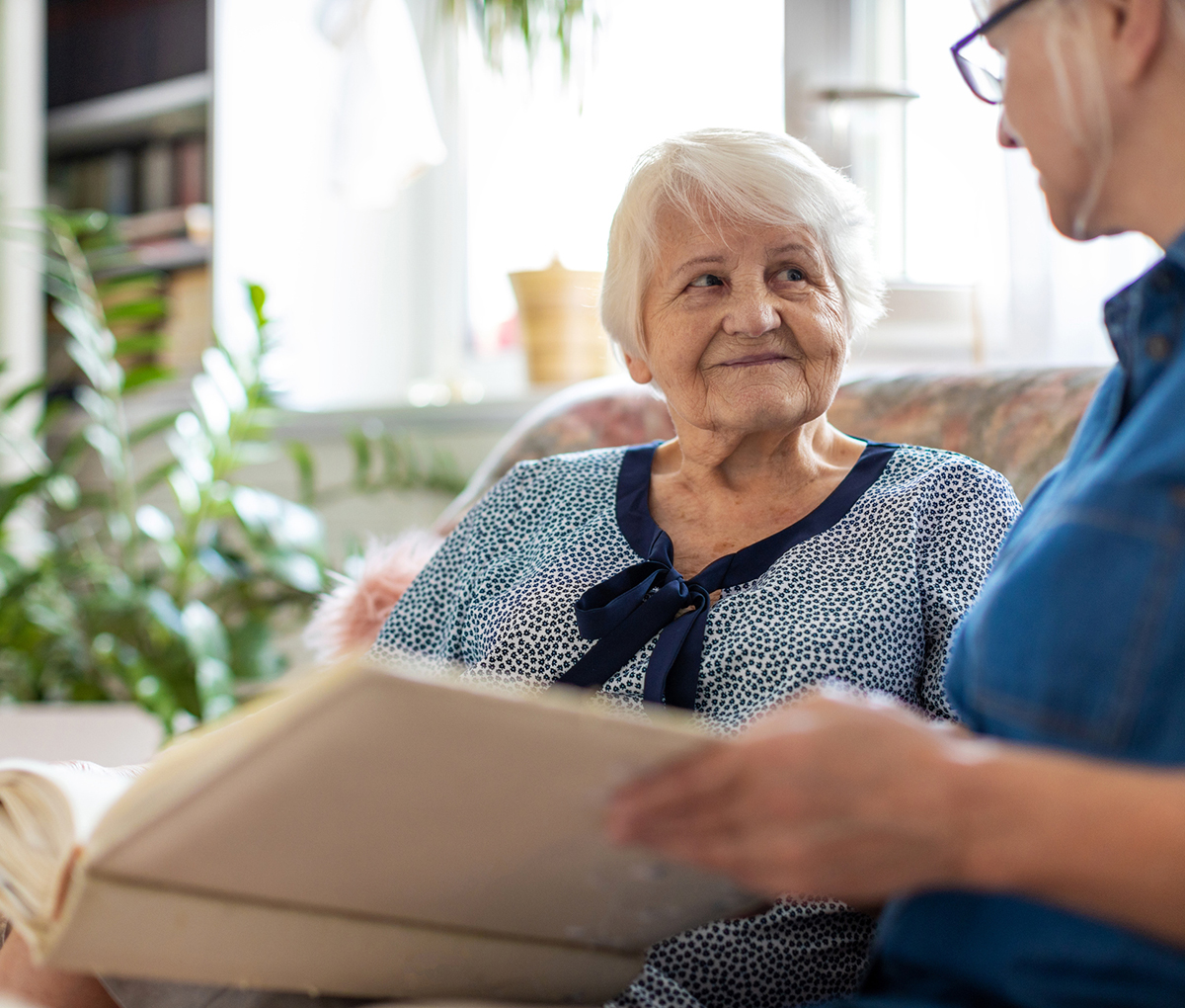 Senior woman and her adult daughter looking at photo album together on couch in living room