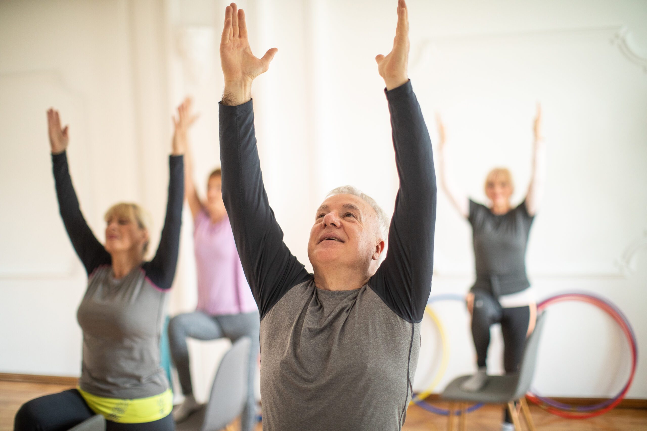 Senior man on yoga class alongside senior women in yoga studio